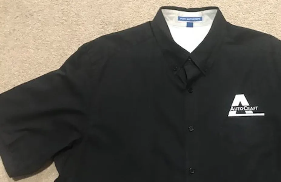 Black collared shirt laid flat on a beige surface.