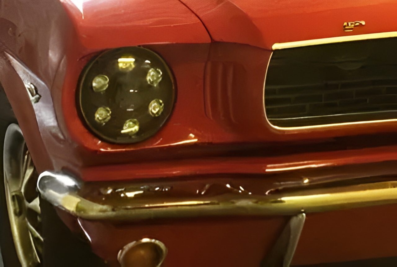 Close-up of a classic red car's front headlight and grille.