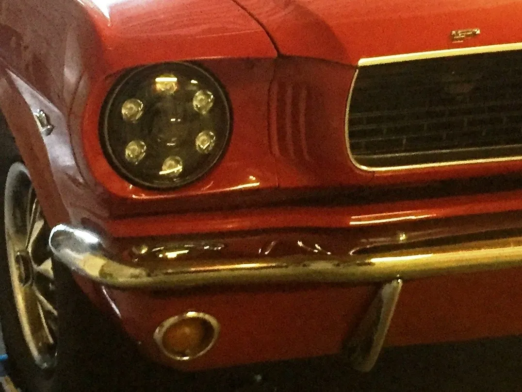 Close-up of a classic red car's front headlight and grille.