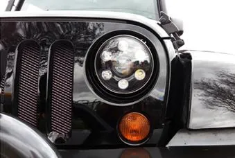 Close-up of a black Jeep's front headlight and amber turn signal.
