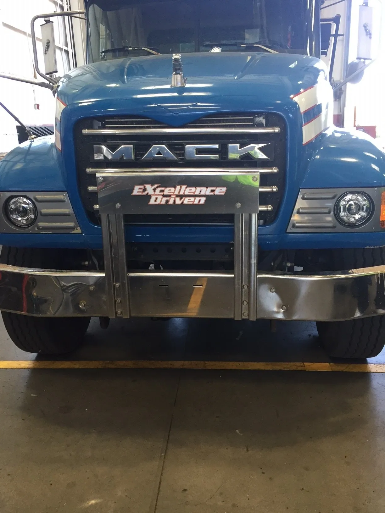 Front view of a blue Mack truck with a sturdy metal grille guard.