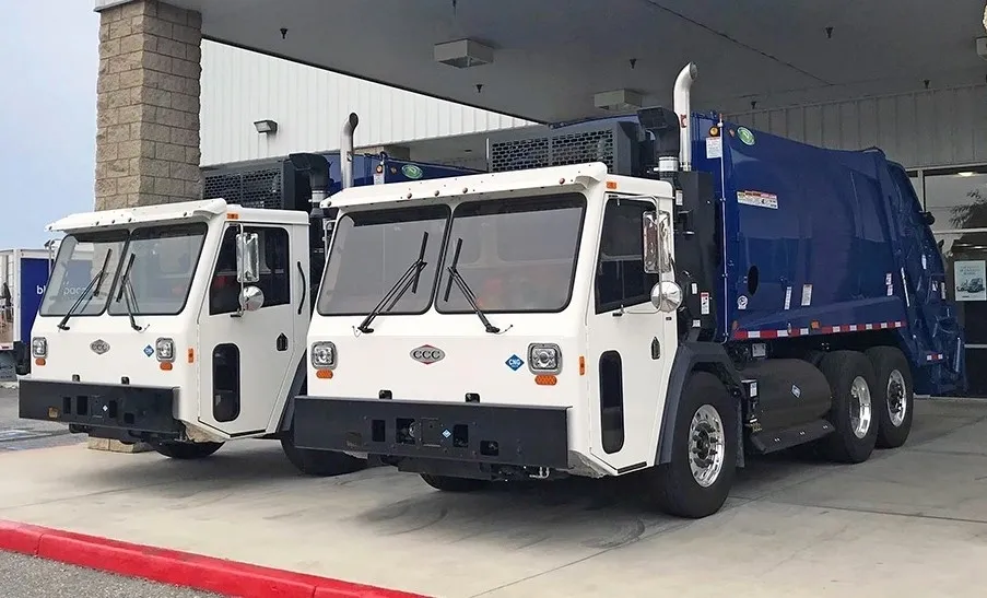 Two white and blue garbage trucks parked side by side.
