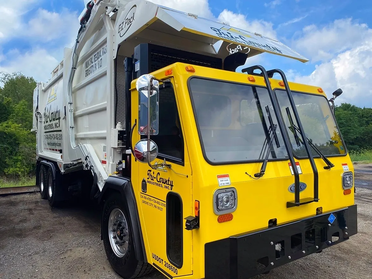 Bright yellow garbage truck parked under a blue sky.